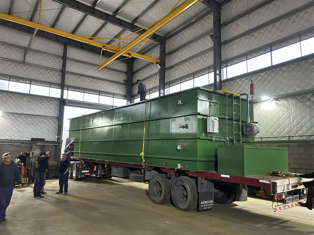 Planta de tratamiento de efluentes cloacales ya terminada y pintada, cargada en un camión dentro de la nave, con tablero de comando, soplador y escalera de acceso