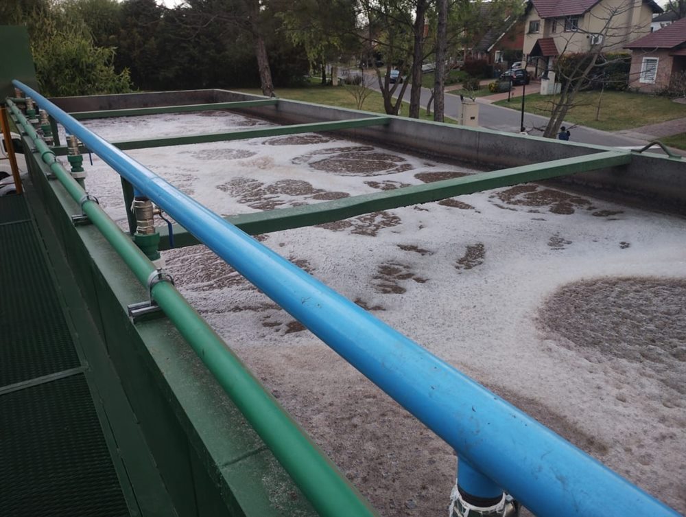 Tanque de aireación en funcionamiento, con la espuma biológica y las cañerías de aire, junto a las casas del barrio