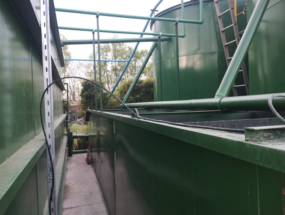 Pasillo entre los tanques de la planta, con cañerías y escalera de acceso