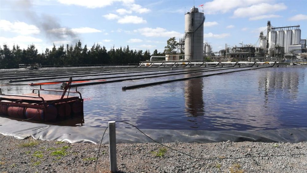 Laguna aireada con un flotante y las mangueras de aireación, frente a una planta industrial
