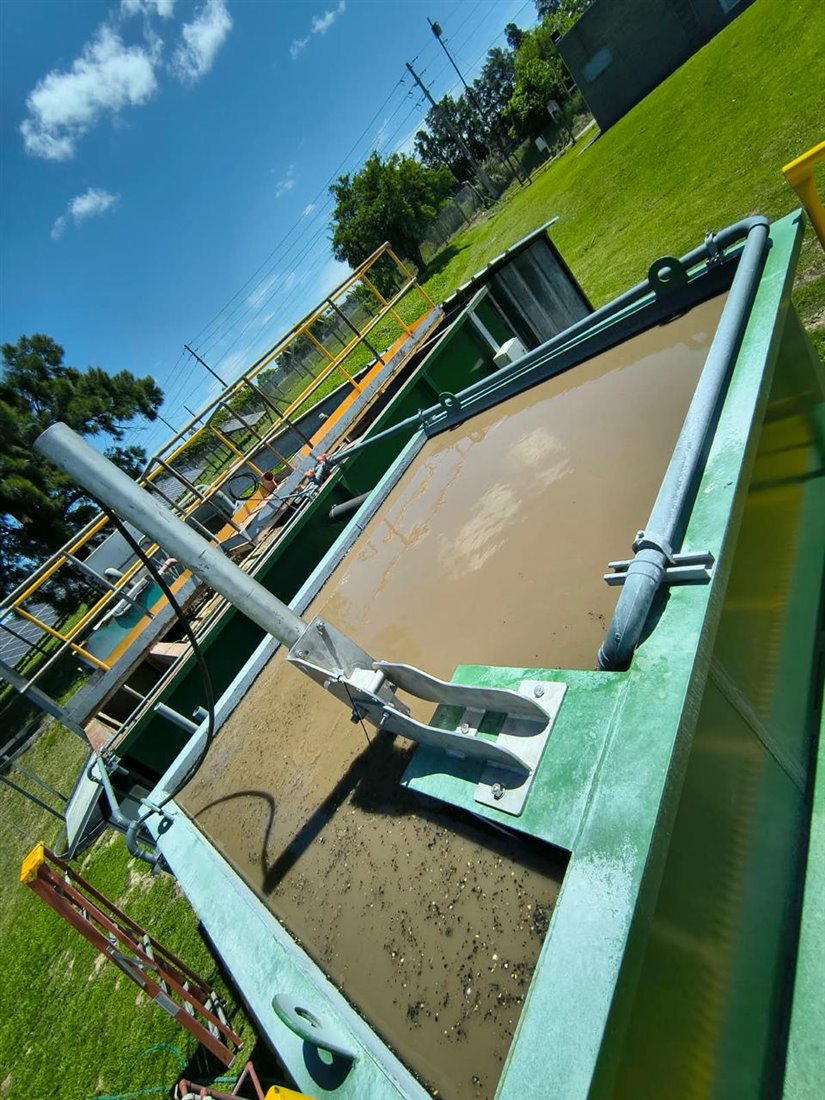Tanque verde de una planta de tratamiento con agua turbia, brazo mecánico y barandas de acceso