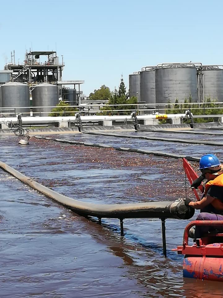 Operario con casco y chaleco revisando una manguera de aireación sobre una laguna