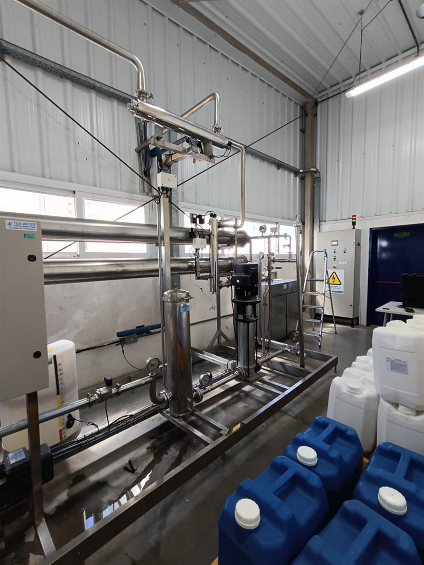 Skid de acero inoxidable con filtro de cartuchos, bomba vertical, lámpara UV y tablero, en una sala de producción