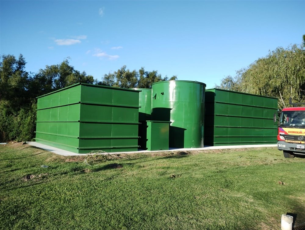 Planta de tratamiento de efluentes instalada: módulos rectangulares y tanque cilíndrico pintados, con camión hidrogrúa